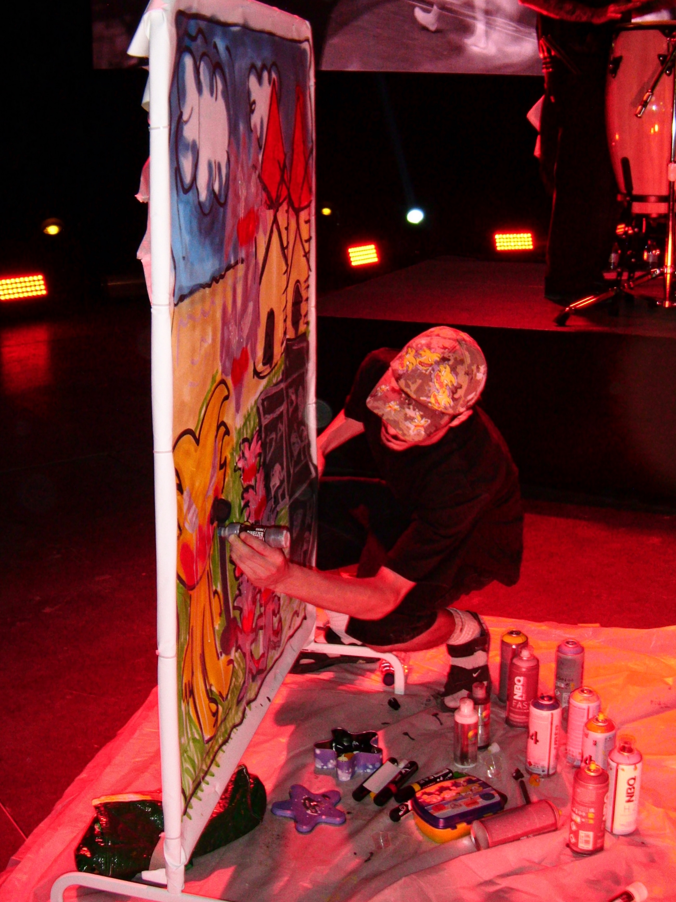Tomás a pintar uma tela em palco, sob luz vermelha, com latas de spray no chão