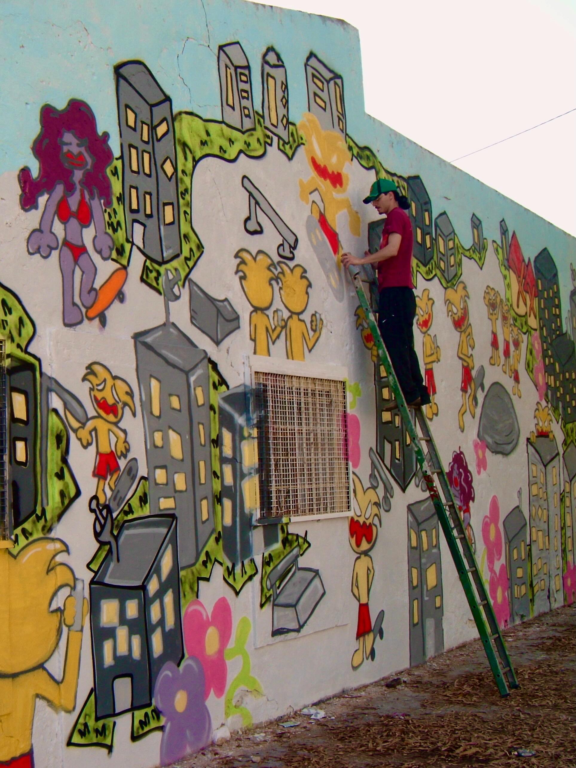 Tomás num escadote a pintar uma parede com prédios e personagens