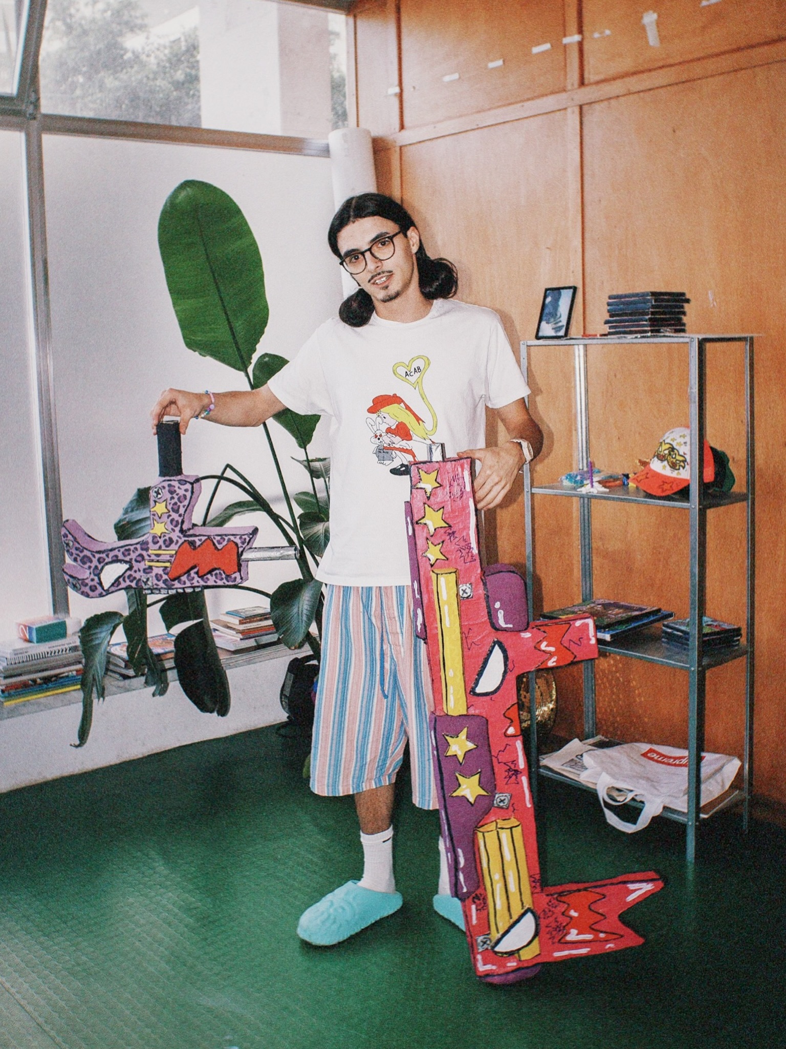 Tomás Santos no atelier, de pé, com duas peças pintadas